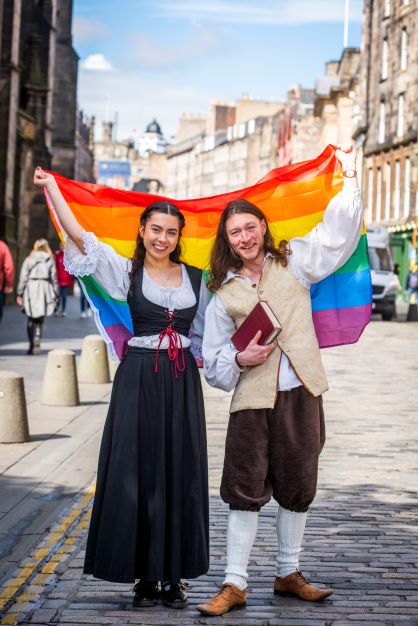 Tour guides dressed as Sophia Jex-Blake and Robert Fergusson for our Pride Month Pride History Tours, holding a Pride flag on Edinburgh's Royal Mile