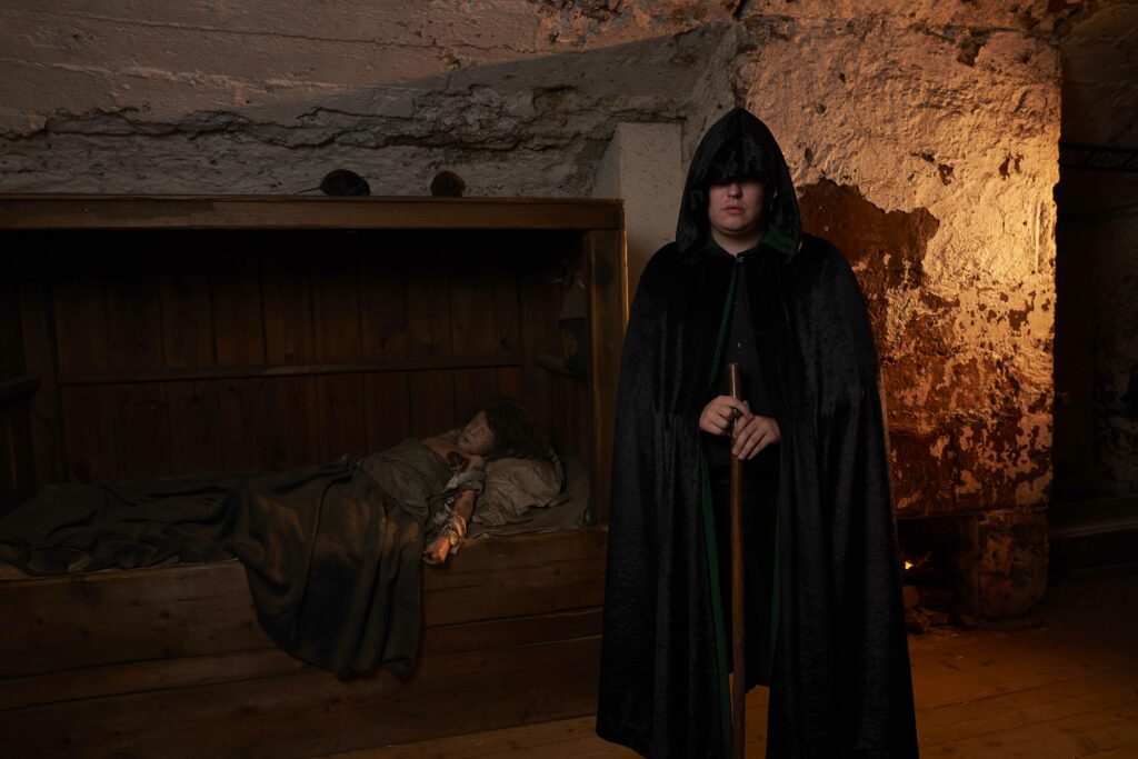 A True Crime guide dressed in a hooded black robe and holding a staff at the real mary king's close. 