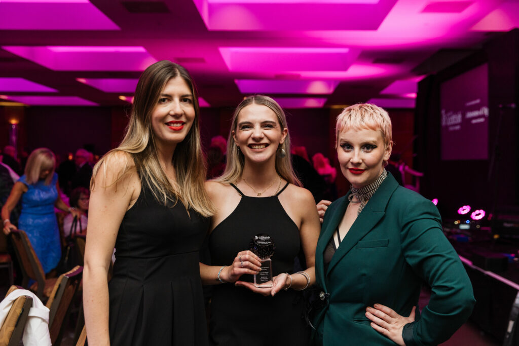 Two people in black dresses (left) and one in teal green suit in a pink ceilinged room at the Scottish Thistle Awards 2023
